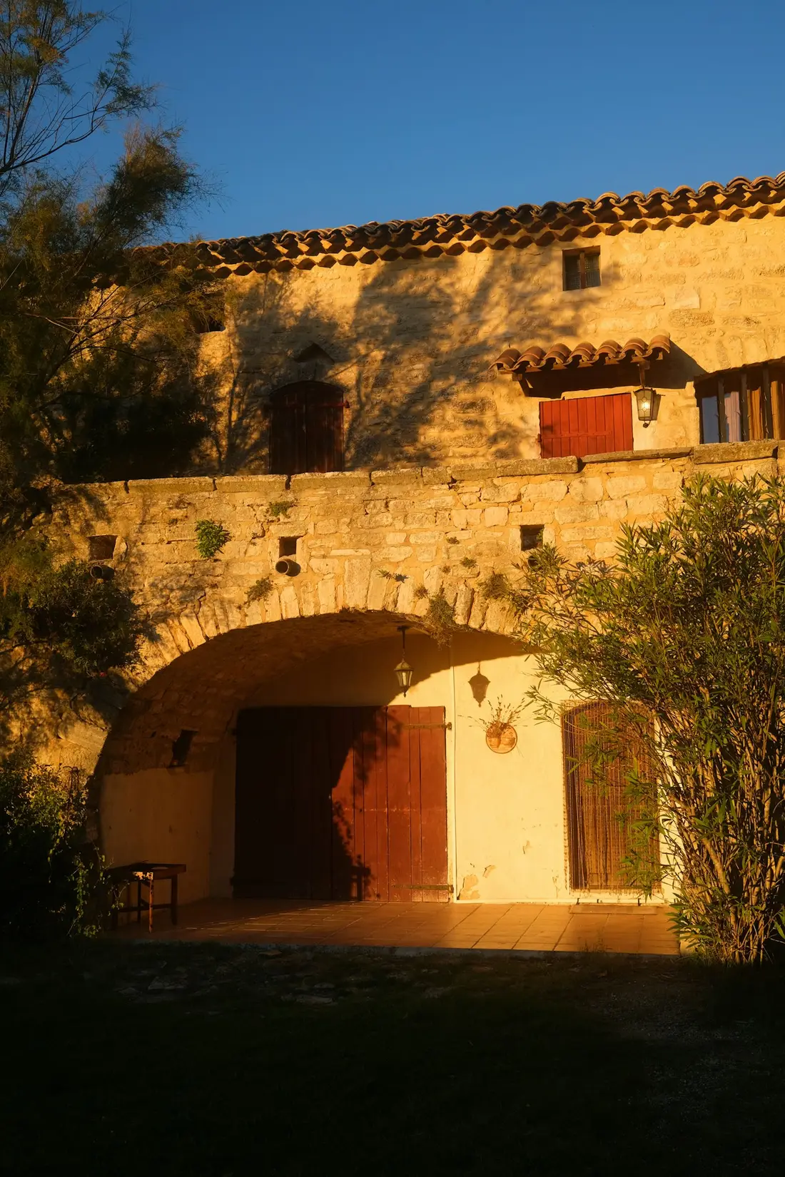 Façade de bastide dorée par le soleil couchant, grande porte en arc.