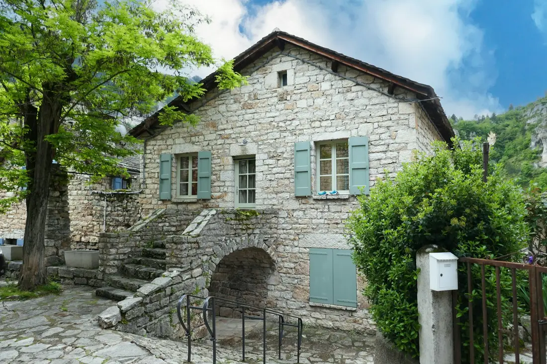 Mas en pierre avec escalier extérieur et volets gris.
