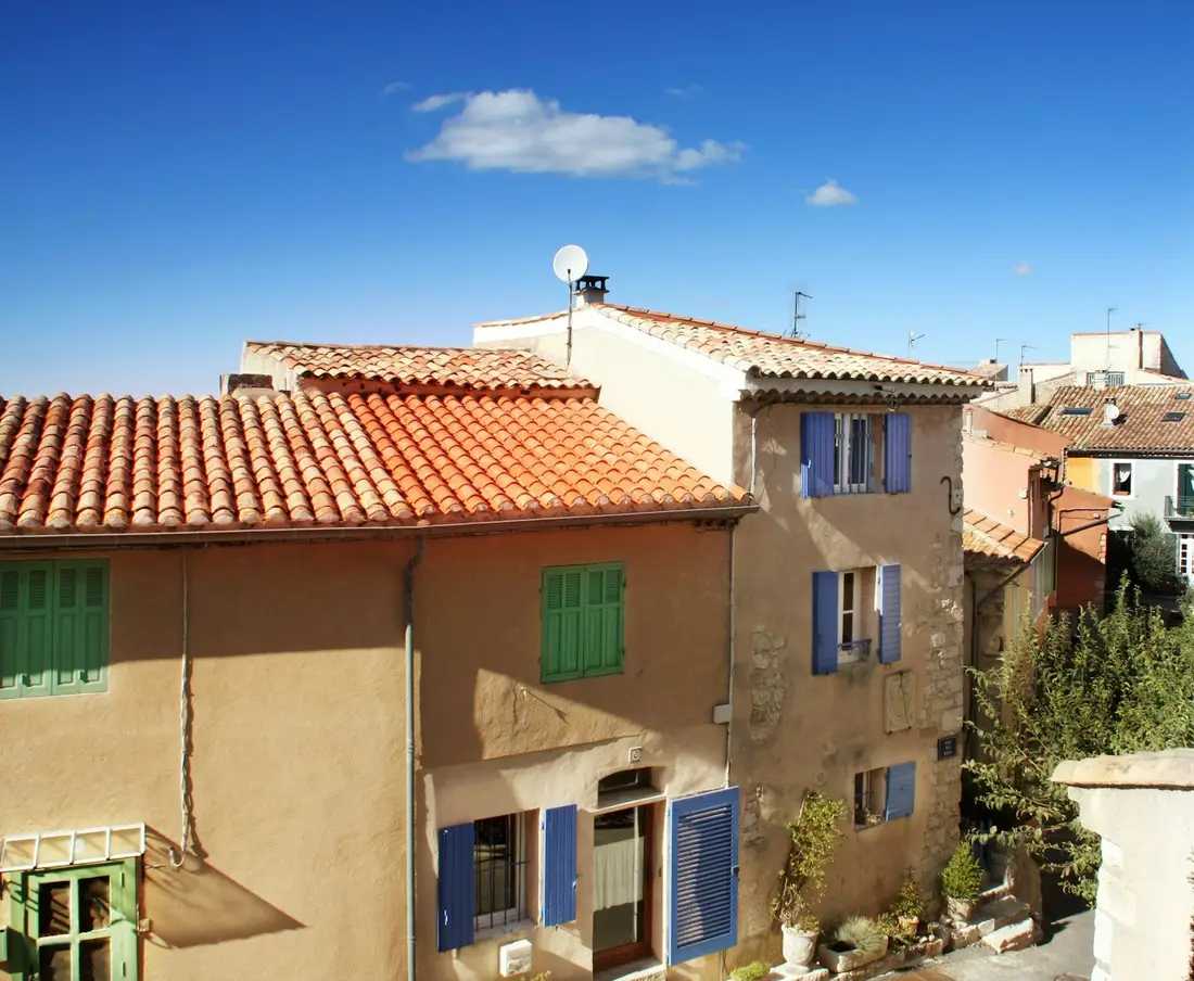 Maisons de village aux enduits ocre et volets bleus, toits de tuiles.